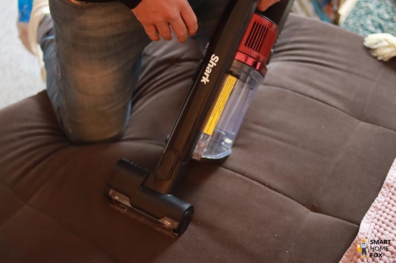 The Shark Anti Hair Wrap hand hoover is seen removing pet hair from furniture.